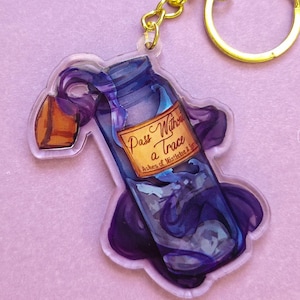 Könnte beinhalten: Ein klarer Acryl-Schlüsselanhänger mit einer blauen Zaubertrankflasche mit Korken und goldener Kette. Die Flasche hat ein Etikett mit der Aufschrift "Pass Without a Trace". Das Design umfasst lila Wirbel auf helllila Hintergrund.