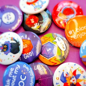 Puede incluir: Una colección de botones redondos de colores con varios diseños y textos. Algunos botones presentan dados, un gato, un bufón y el texto "#1 blorbo enjoyer".