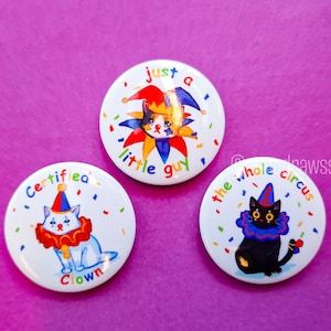 May include: Three round white buttons with colorful confetti and cartoon cats dressed as clowns. The text on the buttons reads "Just a little guy", "Certified Clown", and "The whole circus".