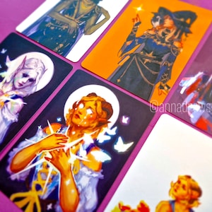 Puede incluir: Seis cartas ilustradas con personajes de fantas&iacute;a. Las cartas est&aacute;n impresas sobre un fondo blanco con un borde morado. Los personajes son una mujer con el pelo largo y blanco, una mujer con el pelo largo y rubio, una mujer con el pelo largo y negro, una mujer con el pelo largo y marr&oacute;n, y una mujer con el pelo corto y marr&oacute;n. Las cartas son de diferentes tama&ntilde;os y formas.
