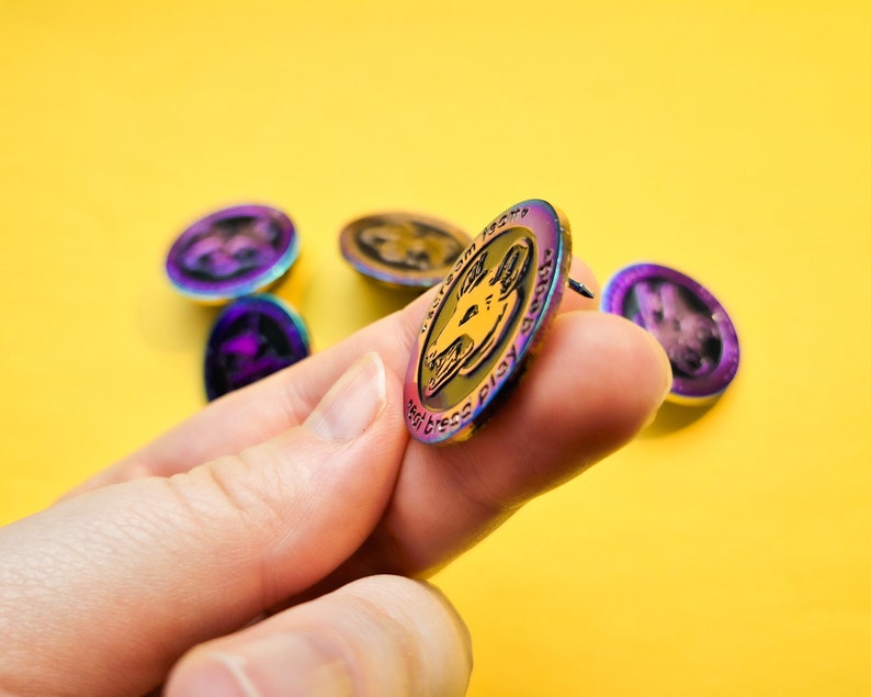 Op de afbeelding: Een regenboogkleurige, iriserende emaille pin met een zwart-witte illustratie van een hondenkop. De pin heeft de tekst "The Goodest Boy" rond de rand.