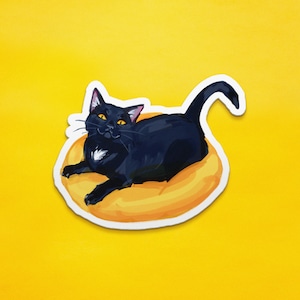 May include: A black cat with yellow eyes is curled up in a yellow donut-shaped bed. The cat is looking directly at the viewer.