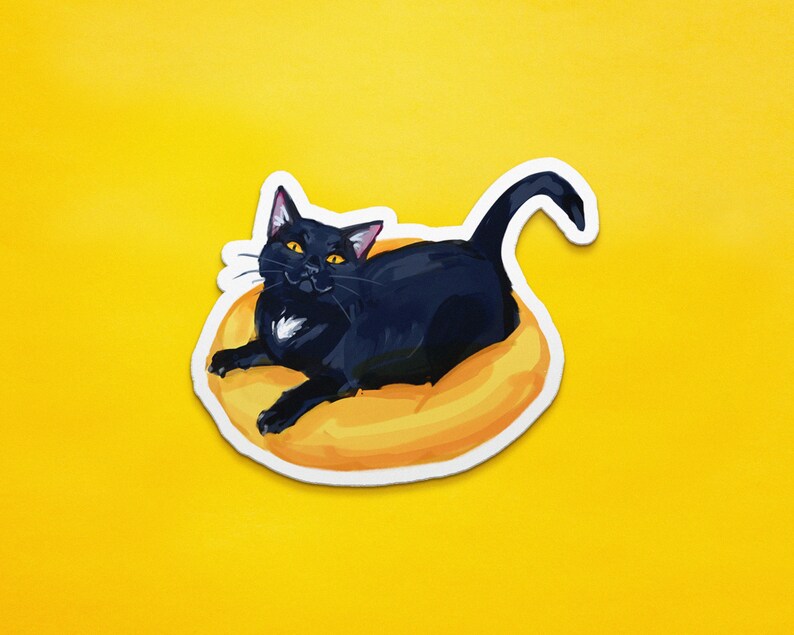 May include: A black cat with yellow eyes is curled up in a yellow donut-shaped bed. The cat is looking directly at the viewer.