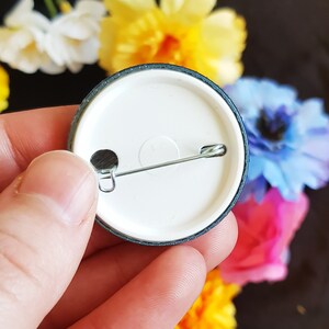 May include: The back of a round, black and white button with a silver safety pin attached. The button has a white center and a black outer ring.