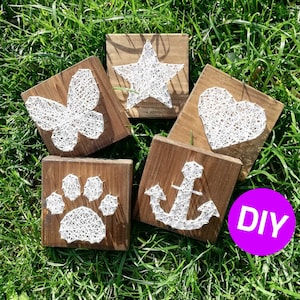 Könnte beinhalten: Fünf Holzplaketten mit String-Art-Designs. Die Designs umfassen einen Schmetterling, einen Stern, ein Herz, einen Anker und einen Pfotenabdruck. Die Plaketten sind alle braun und haben einen rustikalen Look. Die String-Art ist weiß und erzeugt ein schlichtes, modernes Design. Die Plaketten sind in einem Halbkreis auf einem Bett aus grünem Gras angeordnet. Das Wort "DIY" ist in weißen Buchstaben auf einem lila Kreis in der unteren rechten Ecke des Bildes geschrieben.