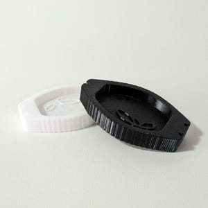 Könnte beinhalten: Zwei 3D-gedruckte Tabletts, eines in Weiß und eines in Schwarz, werden gezeigt. Die Tabletts haben ein Blattdesign und eine geriffelte Außenseite. Das schwarze Tablett ist abgewinkelt und zeigt sein Inneres. Das weiße Tablett liegt auf der Seite.
