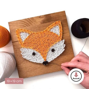 Könnte beinhalten: Handgefertigte String-Art-Fuchs auf einer Holzplatte, 19 x 19 cm groß. Der Fuchs ist mit orangefarbenem, weißem und schwarzem Faden gestaltet. Das Bild zeigt das Kunstwerk mit Garnrollen und einer Hand, die am Faden arbeitet.