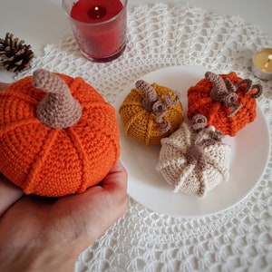 May include: Four crocheted pumpkins in orange, yellow, and cream colors. The pumpkins are sitting on a white crocheted doily.