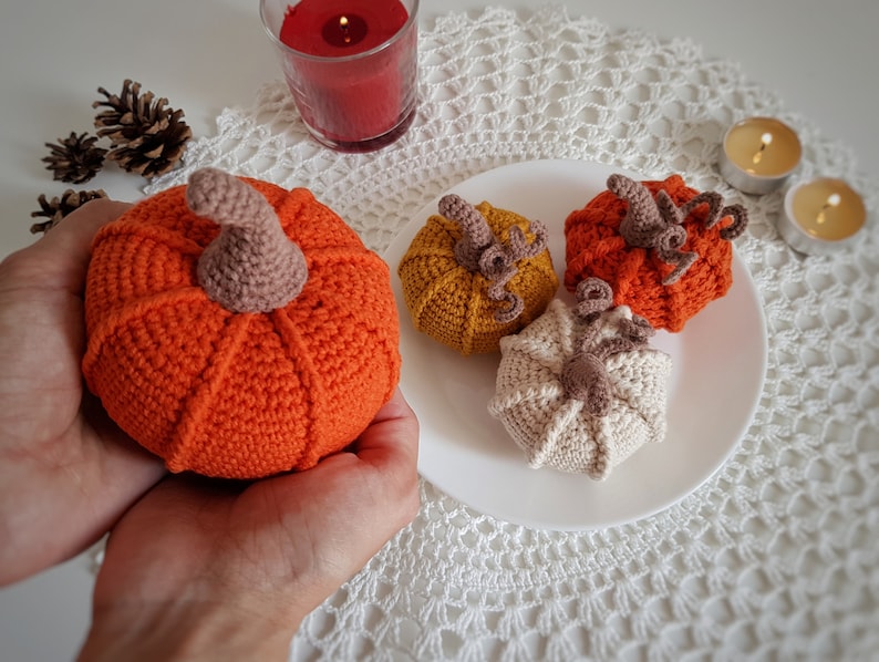 May include: Four crocheted pumpkins in orange, yellow, and cream colors. The pumpkins are sitting on a white crocheted doily.