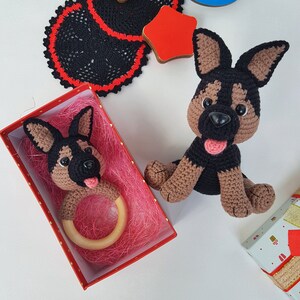 K&ouml;nnte beinhalten: Zwei geh&auml;kelte Spielzeug-Deutscher Sch&auml;ferhunde. Einer ist ein gr&ouml;&szlig;eres Pl&uuml;schtier und der andere ein kleineres Spielzeug mit einem Holz-Bei&szlig;ring. Beide Spielzeuge sind braun und schwarz mit schwarzen Nasen und Zungen.