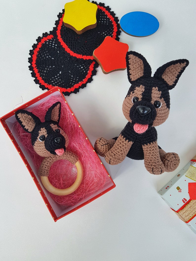 K&ouml;nnte beinhalten: Zwei geh&auml;kelte Spielzeug-Deutscher Sch&auml;ferhunde. Einer ist ein gr&ouml;&szlig;eres Pl&uuml;schtier und der andere ein kleineres Spielzeug mit einem Holz-Bei&szlig;ring. Beide Spielzeuge sind braun und schwarz mit schwarzen Nasen und Zungen.