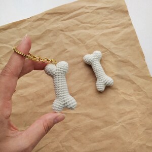 May include: Two white crocheted bone-shaped keychains. One keychain is attached to a gold chain.
