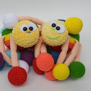 Pu&ograve; includere: Due giocattoli di peluche all'uncinetto a forma di ragno con palline colorate attaccate alle loro gambe. I ragni hanno facce gialle e bianche con occhi neri e sorrisi verdi.