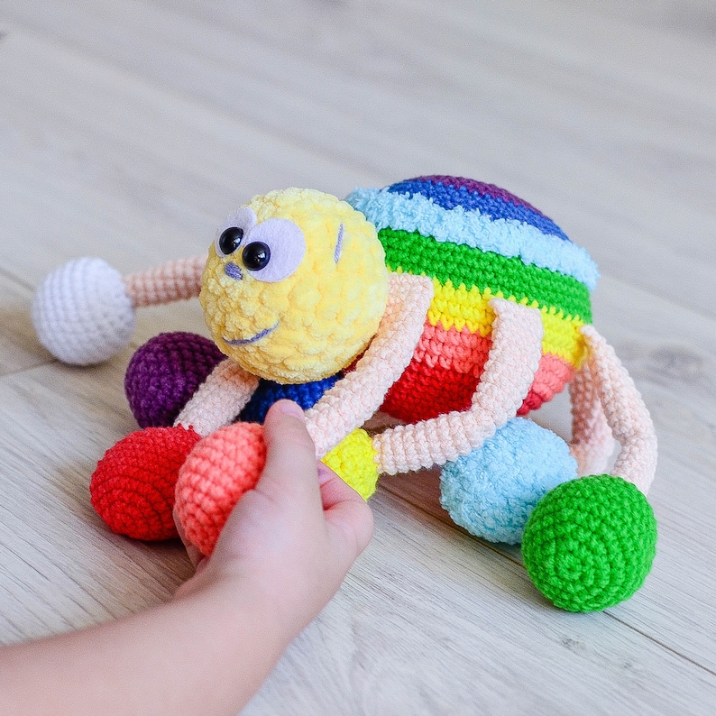 Pu&ograve; includere: Un giocattolo ragno all'uncinetto colorato con una testa gialla e gambe arcobaleno. Il ragno ha grandi occhi neri e un sorriso amichevole. Il giocattolo &egrave; perfetto per la sala giochi o la cameretta di un bambino.