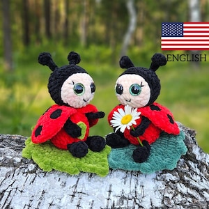 Pode incluir: Dois brinquedos de pelúcia de joaninha de crochê sentados em uma folha verde. As joaninhas têm cabeça preta, corpo vermelho com manchas pretas e olhos grandes e brilhantes. Uma joaninha está segurando uma margarida branca.