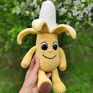 May include: A crocheted banana plush toy with a smiling face and brown feet. The banana is yellow with a white crocheted top.