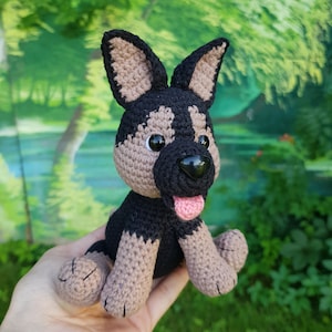 K&ouml;nnte beinhalten: Ein geh&auml;keltes Stofftier in Form eines Hundes mit schwarzem und braunem Fell, schwarzen Augen und einer rosa Zunge. Der Hund sitzt mit gekreuzten Beinen.