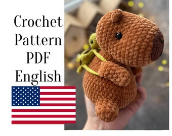 May include: A handmade brown crochet capybara plushie with a small green turtle backpack. The plushie has black eyes and a textured, soft appearance. The image also includes the text "Crochet Pattern PDF English" and the American flag.
