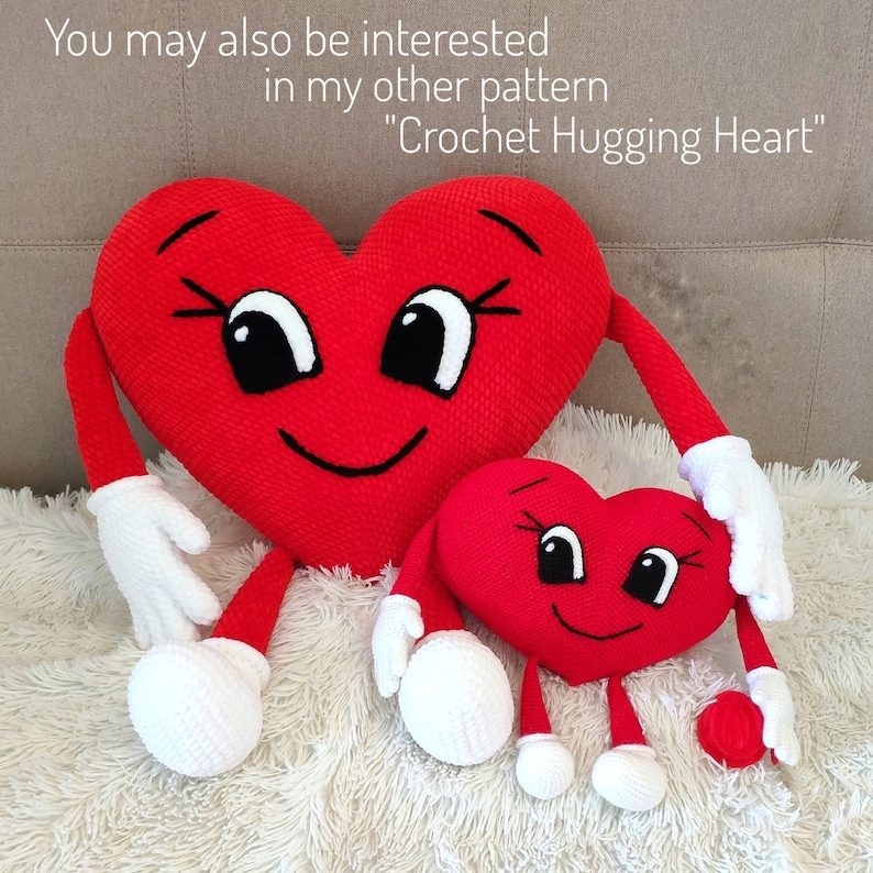 May include: Two crocheted red heart-shaped plush toys with smiling faces and white arms and legs. The larger heart is holding the smaller heart with one arm.