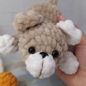 May include: A crocheted plush toy dog with brown and white fur, black eyes, and a black nose. The dog is lying on its side with its head tilted up.