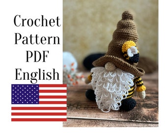 May include: Crochet pattern PDF in English for a bee gnome amigurumi. The gnome is wearing a brown hat with a yellow and black bee design, a black and yellow striped shirt, and a white beard. The gnome is sitting on a wooden surface.