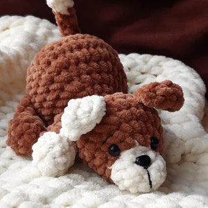 May include: A brown crocheted dog toy with white accents, lying on a white crocheted blanket.