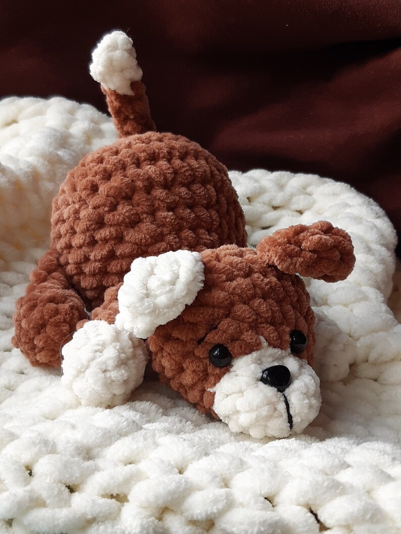 May include: A brown crocheted dog toy with white accents, lying on a white crocheted blanket.