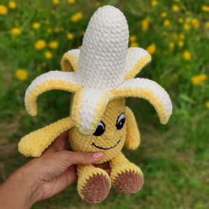 May include: A crocheted banana plush toy with a smiling face and brown feet. The banana is yellow with a white crocheted top.