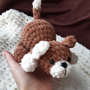 May include: A brown and white crocheted dog toy with black eyes. The toy is made of soft, fuzzy yarn and has a white tail.
