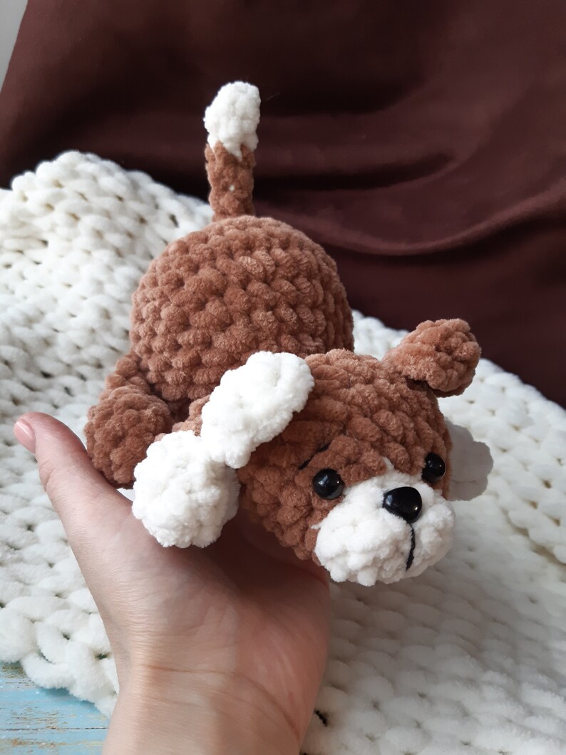 May include: A brown and white crocheted dog toy with black eyes. The toy is made of soft, fuzzy yarn and has a white tail.