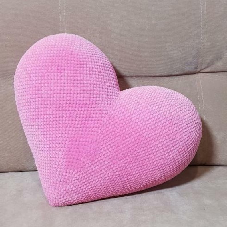 May include: A pink heart-shaped pillow made of soft, textured fabric. The pillow is perfect for adding a touch of love and comfort to any room.