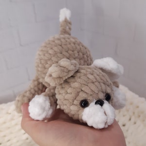 May include: A crocheted plush toy dog with brown fur and white accents. The dog has black eyes and a white nose.
