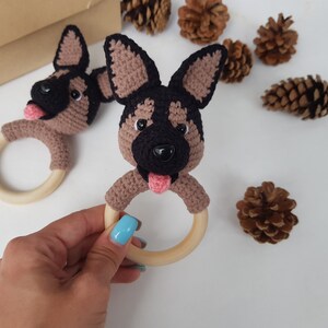 K&ouml;nnte beinhalten: Zwei geh&auml;kelte braune und schwarze Sch&auml;ferhund-Kopf-Bei&szlig;ringe mit rosa Zungen und schwarzen Augen, die an Holzringen befestigt sind.