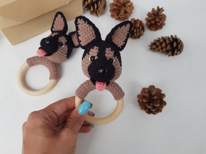 K&ouml;nnte beinhalten: Zwei geh&auml;kelte braune und schwarze Sch&auml;ferhund-Kopf-Bei&szlig;ringe mit rosa Zungen und schwarzen Augen, die an Holzringen befestigt sind.