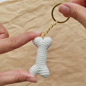 May include: White crocheted bone-shaped keychain with a gold chain and ring.
