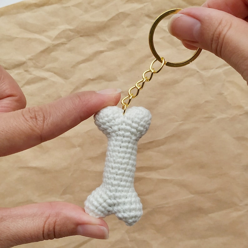 May include: White crocheted bone-shaped keychain with a gold chain and ring.