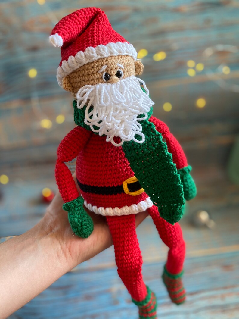 May include: Crocheted Santa Claus doll with a red hat, white beard, green scarf, and red and white striped socks.