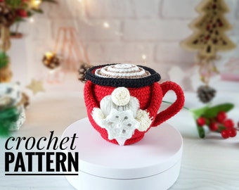 May include: A red crocheted mug with a black rim and a white snowflake design. The mug has a handle and is filled with a brown and white crocheted design. The words "crochet PATTERN" are in the image.
