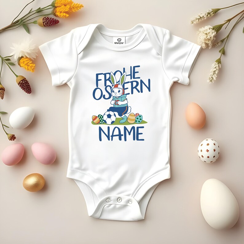 May include: White baby onesie with a blue and white cartoon bunny holding a soccer ball and surrounded by Easter eggs. The text "Frohe Ostern" is above the bunny and "NAME" is below the bunny.