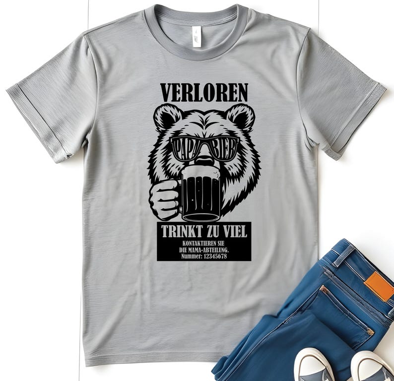 May include: A light grey t-shirt with a black graphic of a bear wearing sunglasses and holding a beer mug. The text on the shirt reads "VERLOREN", "PAPA BIER", and "TRINKT ZU VIEL". Below the bear is a black rectangle with additional text and a phone number.