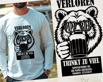 May include: A long-sleeve white shirt featuring a black and white graphic of a bear wearing sunglasses that read "PAPA BIER" and holding a beer mug. The text "VERLOREN" and "TRINKT ZU VIEL" are above and below the bear graphic, respectively.