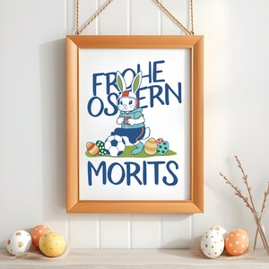 May include: A framed print with a white bunny wearing a helmet and holding a soccer ball. The text on the print reads "Frohe Ostern Morits".