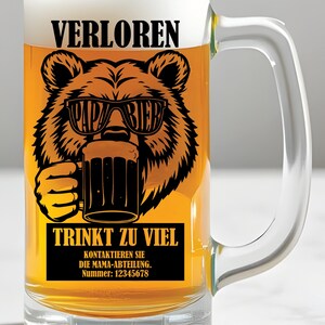 May include: A clear glass beer mug filled with beer and foam. The mug has a black graphic of a bear wearing sunglasses that say "PAPA BIER" and holding a beer mug. Text on the mug reads "VERLOREN" and "TRINKT ZU VIEL".