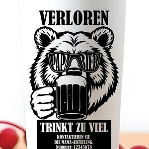May include: White travel mug featuring a black bear graphic wearing sunglasses and holding a beer stein. The mug has German text: "VERLOREN" and "TRINKT ZU VIEL". A humorous gift for beer enthusiasts. The mug is suitable for hot or cold drinks.
