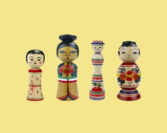 May include: Four traditional Japanese wooden dolls, each with a unique design and painted details. The dolls are standing on a yellow background.
