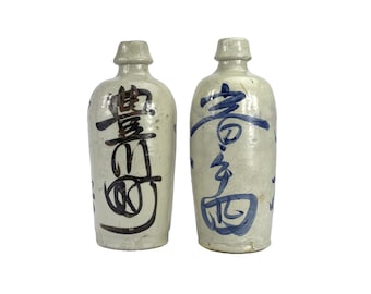May include: Two antique ceramic bottles with a cream-colored glaze. Each bottle features dark blue and black calligraphy. The bottles have a rounded body and a narrow neck. The bottles are displayed against a white background.