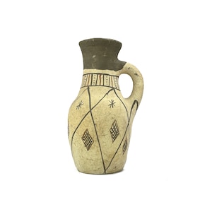 May include: A small, hand-painted ceramic jug with a brown, white, and black geometric design. The jug has a rounded body and a small handle.