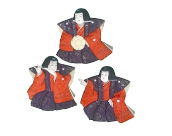 May include: Three traditional Japanese dolls wearing colorful kimonos with intricate patterns. The dolls are posed in different positions, with one holding a small drum.