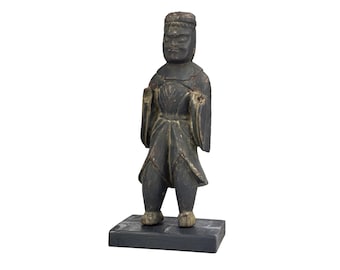 May include: A dark gray wooden figurine of a person in traditional clothing, standing on a rectangular base. The figure has a stern expression and is wearing a hat and long sleeves. The statue is approximately 6 inches tall.