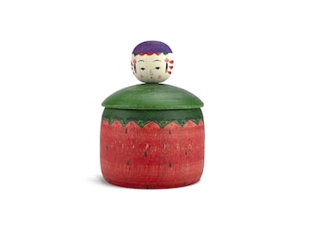 May include: A wooden box with a watermelon design and a painted wooden doll head on top. The box has a green lid and the watermelon design is red with black seeds.